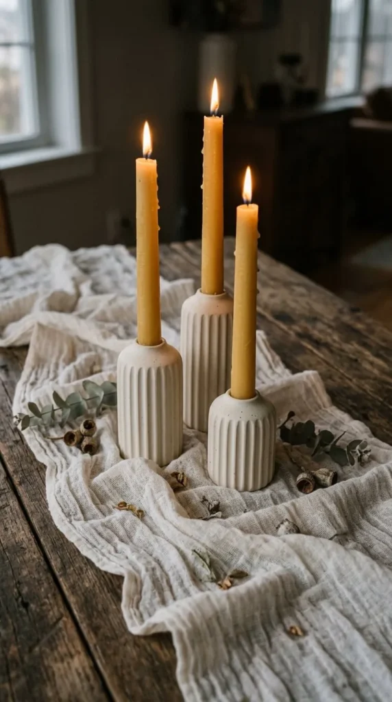 Three lit yellow candles in white holders on wooden table.